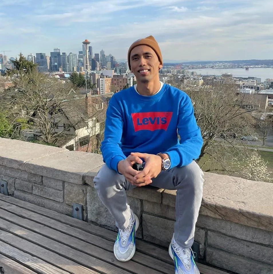 A person in a blue Levi's sweatshirt sits on a stone ledge with a cityscape in the background, holding a small object.