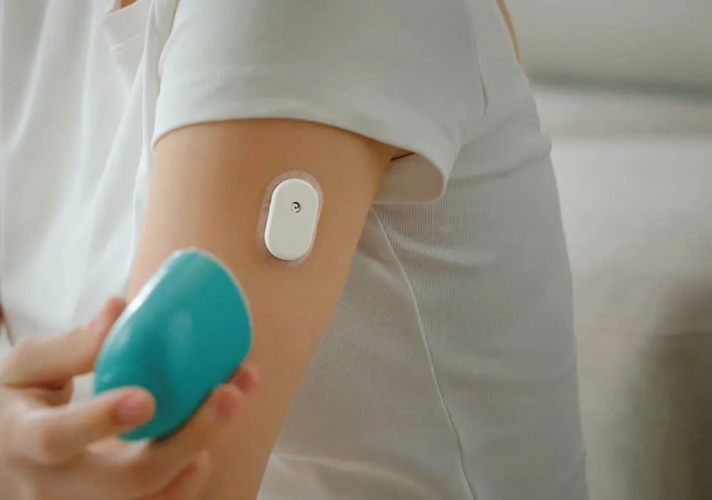 A person using a blue device on their arm with a Sibionics glucose monitor attached. Keywords: Sibionics, glucose monitor, device.