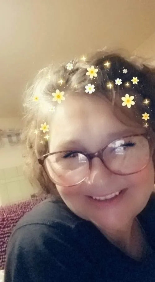 A person with curly hair and glasses, adorned with digital yellow and white flowers and sparkles.