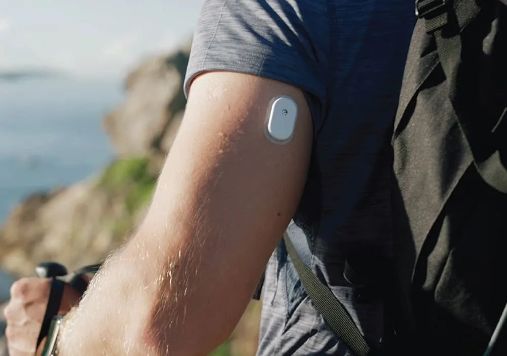 A person wearing a Sibionics glucose monitor on their arm, outdoors with a scenic background.